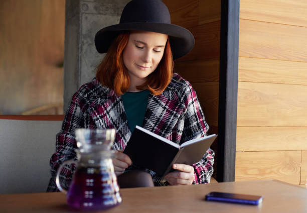 istock Ginger haired female making reading book and drinking tea in cafe. 1142479253