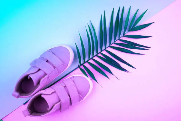 Photo of Sneakers and sprig of palm trees on a trendy color background, top view, summer shoes.