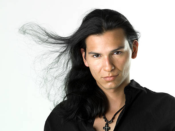 Portrait of gen z young man with long hair looking at camera. Studio shot, gray background.