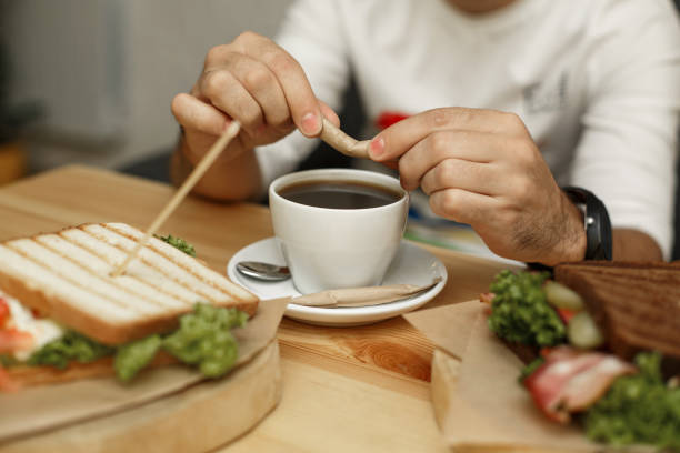 istock Man breaks sugar stick before pour it in coffee cup. Morning breakfast with fresh coffee and juice sandwich 1142492760