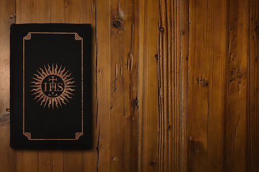 Close-up on black bible with a gilded Christogram of the Society of Jesus (founded in 1540) in its middle.