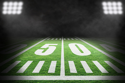Close up of American football field with stadium spotlight on specific 50 yard markings and background smoke with copy space. Fictitious stadium created in Photoshop.