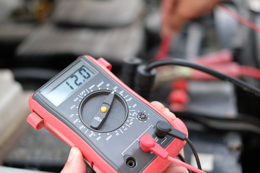 auto mechanic check car battery voltage by voltmeter multimeter at repair service station