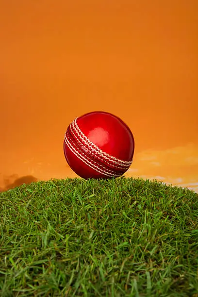 Cricket ball on turf mound against orange sunset.