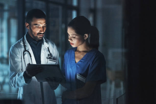 Dedicated to reaching a diagnosis Shot of two young doctors using a digital tablet late at night in a modern hospital working late photos stock pictures, royalty-free photos & images