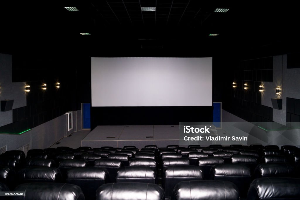 El interior de una sala de cine con asientos de cuero negro y una pantalla blanca. La película no se muestra y no hay gente. - Foto de stock de Color negro libre de derechos