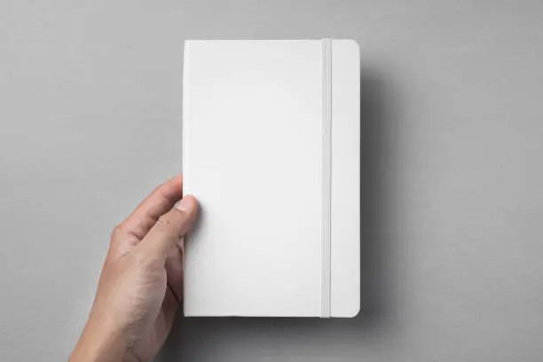 Design concept - top view of close white notebook hold by mans hand on grey background for mockup. real photo, not 3D render