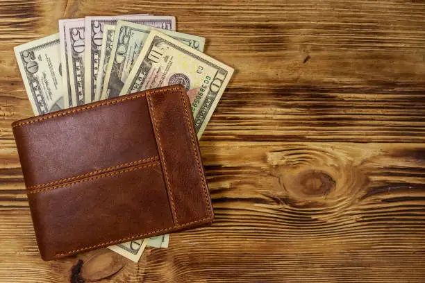 Photo of Brown leather wallet and american dollars on wooden table. Top view