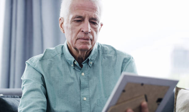 All we have are memories Shot of a thoughtful senior man looking at a picture frame at home mourner photos stock pictures, royalty-free photos & images