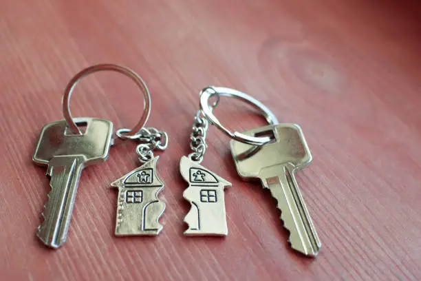 Two keys with splitted or broken key rings with pendant in shape of house divided in two parts on wooden background with copy space. Dividing house when divorce, division of property, real estate heritage.