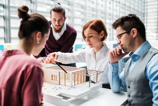 istock Group of young architects with model of a house working in office, talking. 1142548251