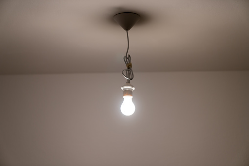 A naked lit light bulb hanging from the ceiling of a dimly lit room