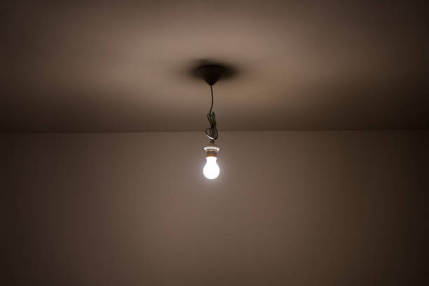 istock naked lit light bulb hanging from the ceiling of a dimly lit room 1142551506