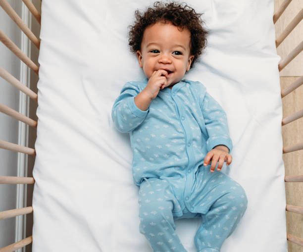 overhead-ansicht eines glücklichen babyjungen, der in einer krippe liegt und pyjamas trägt - babybett stock-fotos und bilder