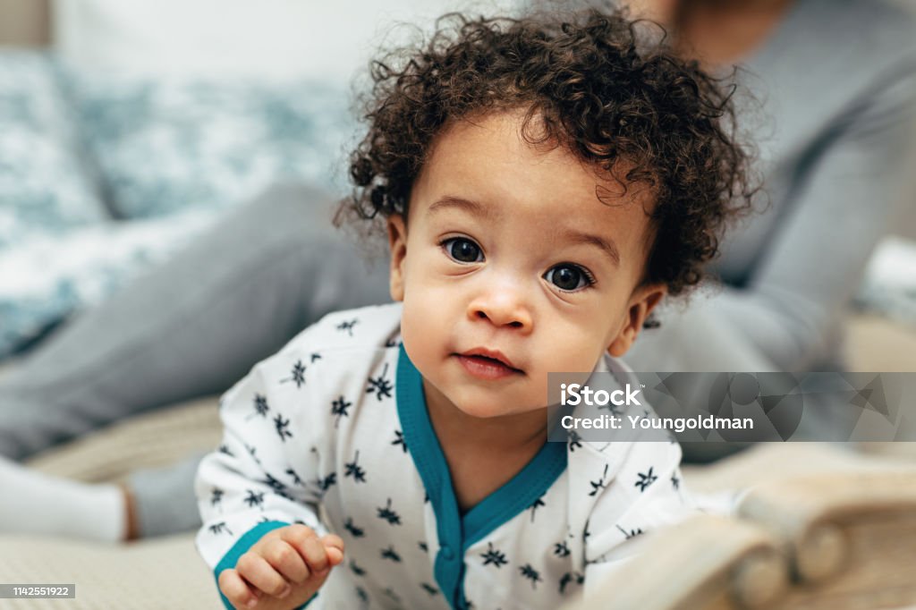 Close up portrait of a curly-haired baby boy crawling on bed Baby - Human Age Stock Photo