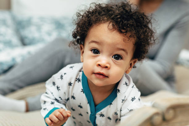 Close up portrait of a curly-haired baby boy crawling on bed stock photo