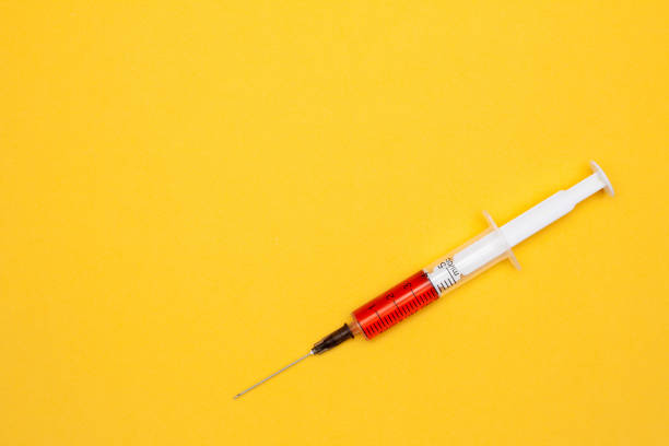 istock Syringe with red liquid (blood) on yellow background with a place under the text 1142554767
