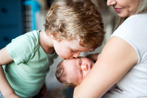 un niño pequeño besando a un hermano recién nacido durmiendo en casa. - baby mother sleeping child fotografías e imágenes de stock