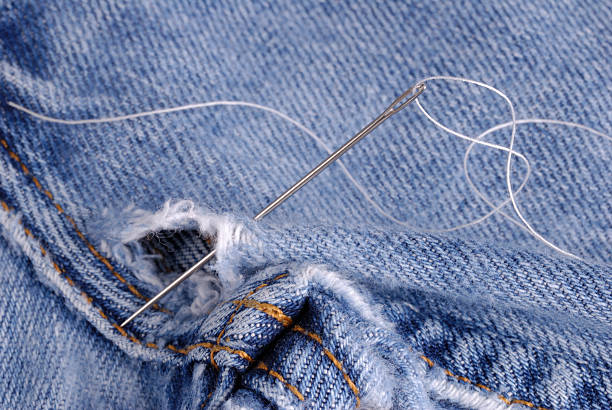 Denim jeans in need of repair with needle and thread Denim jeans in need of repair with needle and thread in position. hole in pants stock pictures, royalty-free photos & images