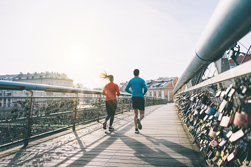 Rear view on  woman and man jogging over bridge at summer morning