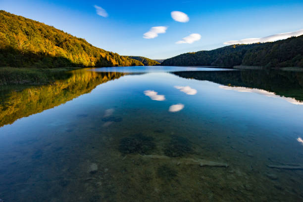 istock Interesting scattered white clouds reflecting in a large upper lake with forested hilly shores in Plitvice National Park in Croatia at dusk in autumn 1142579867