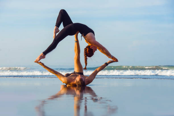 young attractive and beautiful acrobat couple practicing acroyoga exercise concentrated keeping balance practiing yoga on the beach in relaxation and meditation concept and healthy lifestyle young attractive and beautiful acrobat couple practicing acroyoga exercise concentrated keeping balance practiing yoga on the beach in relaxation and meditation concept and healthy lifestyle acrobatic activity stock pictures, royalty-free photos & images