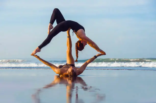 young attractive and beautiful acrobat couple practicing acroyoga exercise concentrated keeping balance practiing yoga on the beach in relaxation and meditation concept and healthy lifestyle