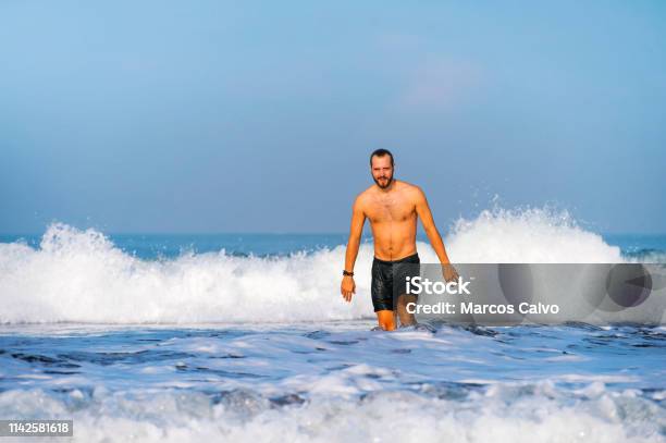 Young Attractive And Happy Man With Beard And Swimming Trunks At Tropical Paradise Desert Beach Alone Playful And Cheerful In Sea Water Enjoying Summer Holidays Destination Isolated Blue Stock Photo - Download Image Now