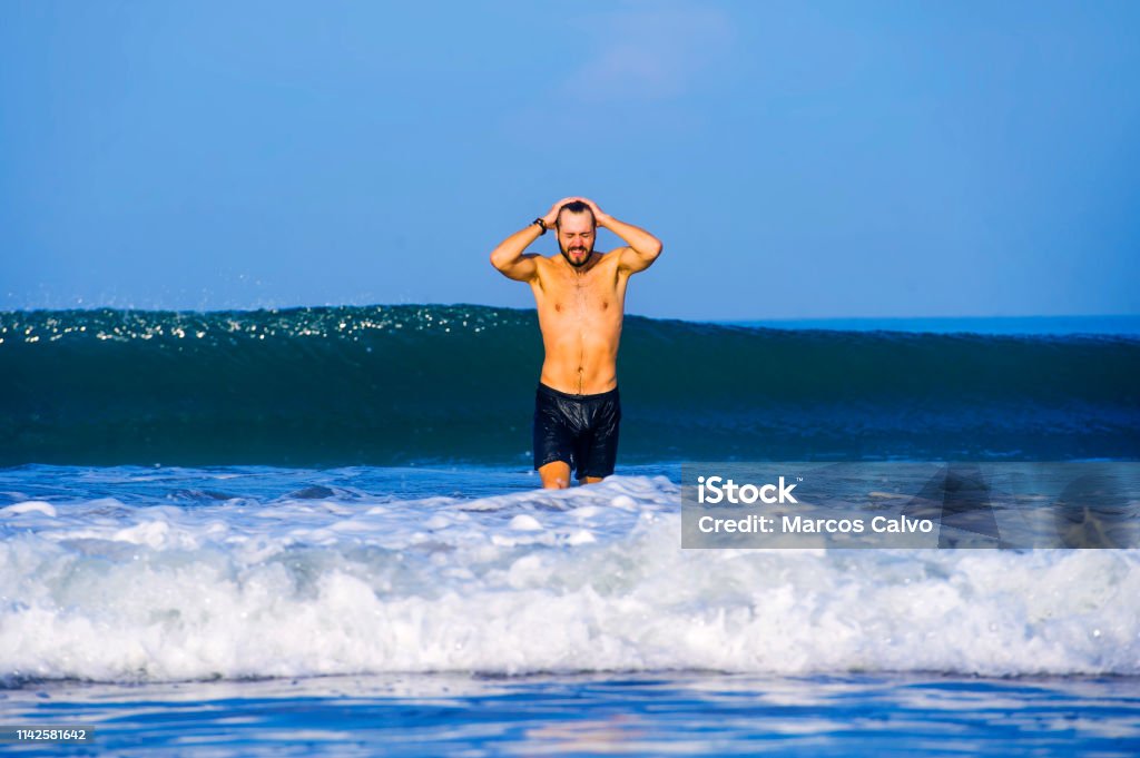 young attractive and happy man with beard and swimming trunks at tropical paradise desert beach alone playful and cheerful in sea water enjoying Summer holidays destination isolated blue 30-39 Years Stock Photo