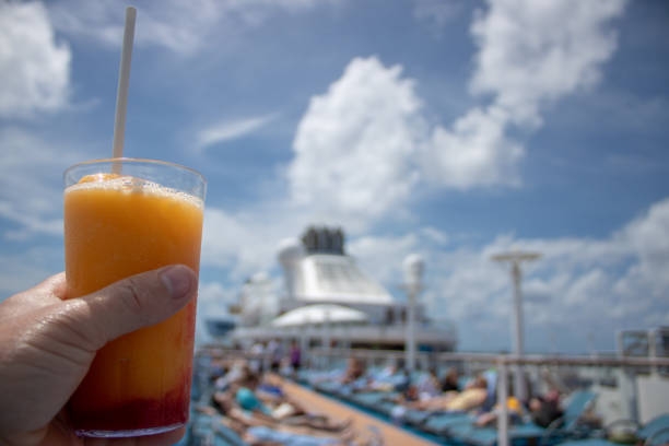 Orange and Mango Cocktail on on a cruise liner being held by a Caucasian mans left hand on beautiful tropical beach. stock photo