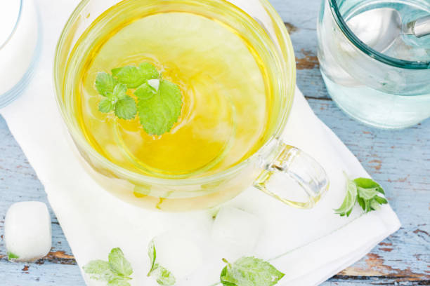 Cold fresh mint leaf tea, mint tea with ice cubes in a glass cup on a wooden table, cold mint beverage, healthcare and healthy eating concept