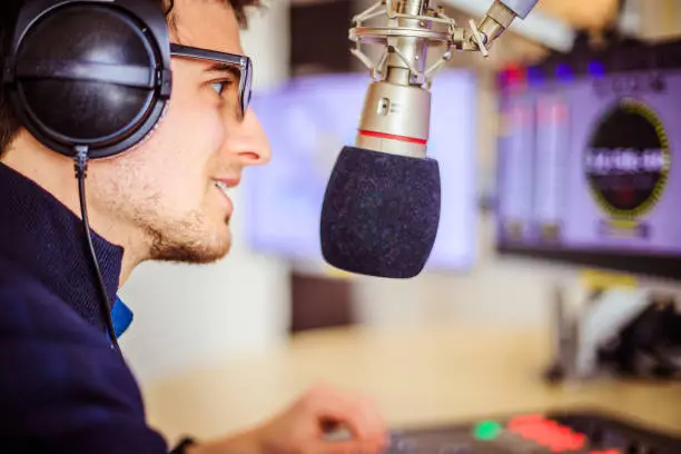 Young man in the broadcasting studio, radio, talking into the microphone