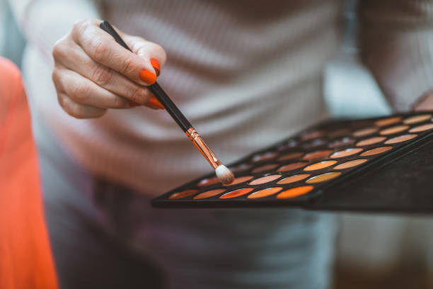 Photo of female Cosmetics consult tells about eyeshadows palette. Young woman holding colorful eye cosmetics swatch. Makeup, beauty, fashion concept. Make-up eye shadows with make-up brush