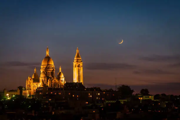 Night view of an illuminated Sacre Coeur on a clear night with the moon in the background. Paris, France.