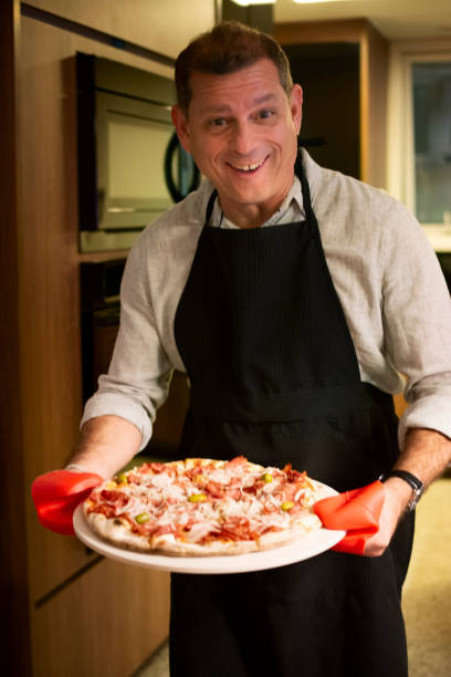 istock Man serving a pizza that just baked in the oven, and looking at camera. 1142594271