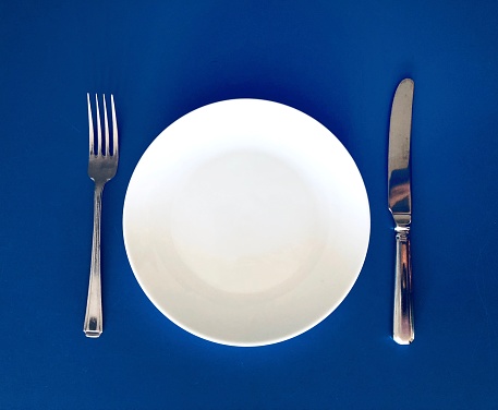 White plate and knife and fork on blue background