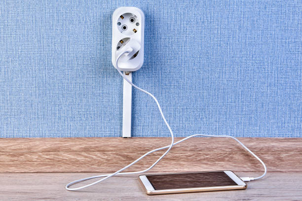 Mobile phone is charging with wall outlet. Smartphone is plugged into the charger which is inserted into a double outlet. battery charger photos stock pictures, royalty-free photos & images