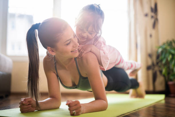 średnio dorosła matka praktykuje jogę z małą córką na jej szczycie, piękna matka i córka trenująca trening domowy - yoga flexibility two people women zdjęcia i obrazy z banku zdjęć