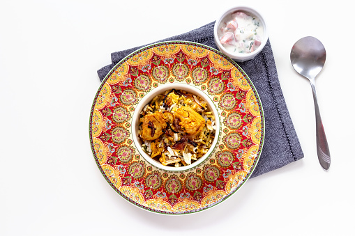 Halal Indian chicken Biryani served with yogurt tomato raita over white background. Selective focus. Top view.