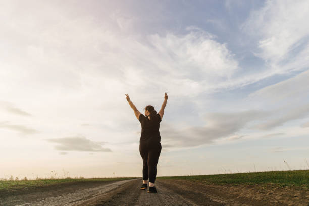 Overweight woman celebrating rising hands to sky Body positive, freedom, high self esteem, confidence, happiness, inspiration, success, positive affirmation. Overweight woman celebrating rising hands to the sky on summer meadow. health motivation stock pictures, royalty-free photos & images
