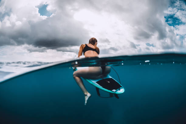 istock Attractive surf girl sit at surfboard in blue ocean 1142622539