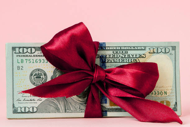 one hundred dollars gift wraped with a red ribbon on pink background one hundred dollars gift wraped with a red ribbon on pink background. giving money stock pictures, royalty-free photos & images