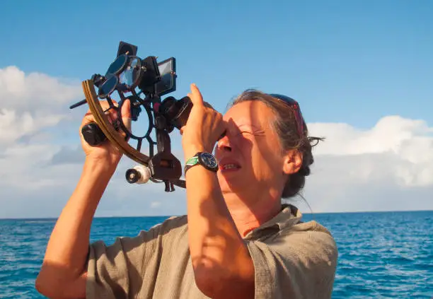 woman as a navigator on board of a sailing yacht, using a sextant as traditional navigation tool for position fixing