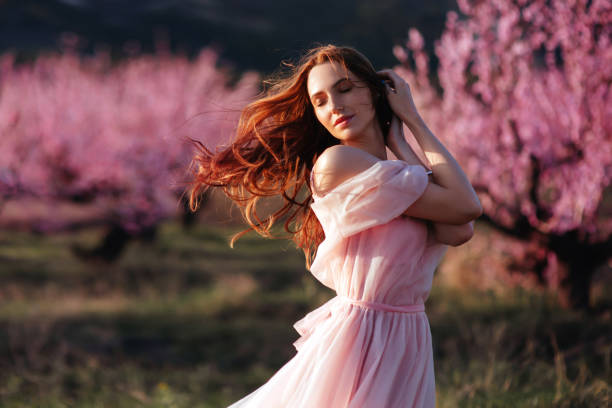 schönes junges mädchen unter dem blühenden rosa baum - beauty beautiful attractive female red hair stock-fotos und bilder