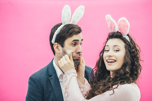 Young beautiful couple standing on a pink background.