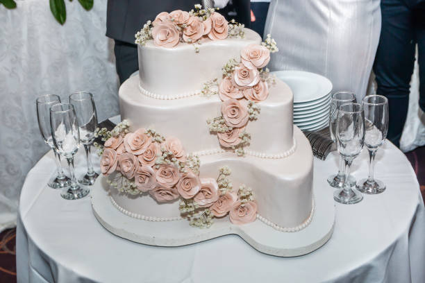 istock Three-tiered white wedding cake decorated with roses and glasses for champagne on restaurant table ready for bride and groom 1142636411