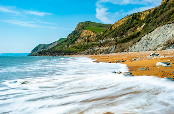 Showing the wave rolling on tto the sands ith the cliffs in the background on a bright sunny day in spring.