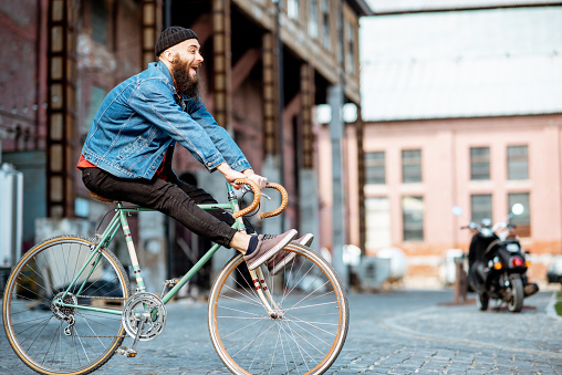 Stylish man as a crazy hipster having fun, riding retro bicycle outdoors on the industrial urban background