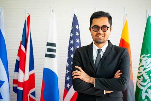 Business or political man with beard is smiling and stand with various international flags.