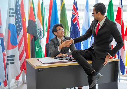 contemporary intercultural delegates shaking hands after successful meeting press conference with microphones, in boardroom office. caucasian and arabic executives signed a bilateral agreement